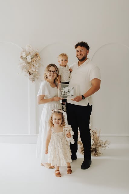 A family of four in a bright studio holding a framed ultrasound photograph