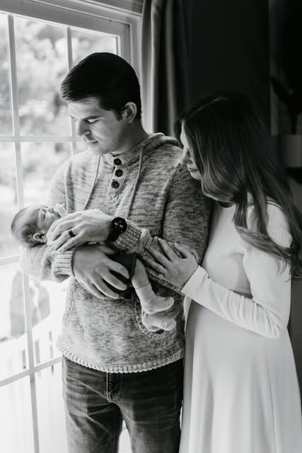 Black-and-white photograph of parents holding their newborn beside a window
